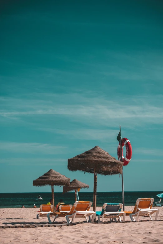 there is a row of chairs on the beach next to some straw umbrellas