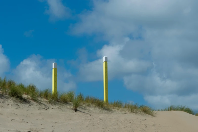 an empty beach covered in sand with two yellow poles