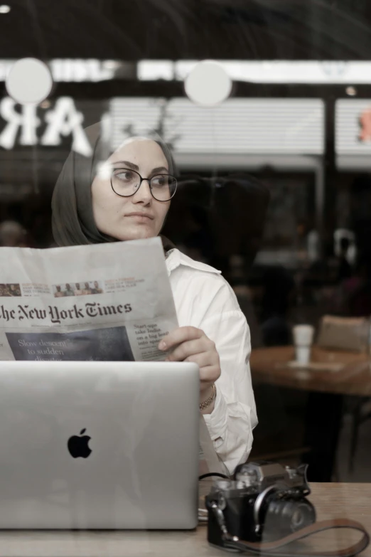 a woman holding an ipad is reading the new york times newspaper