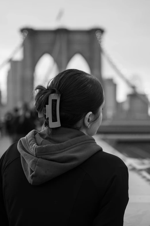 a woman with a pair of hair clips in her ears stands in front of the brooklyn bridge