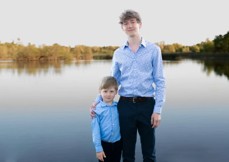 a father and son pose for a picture by the water