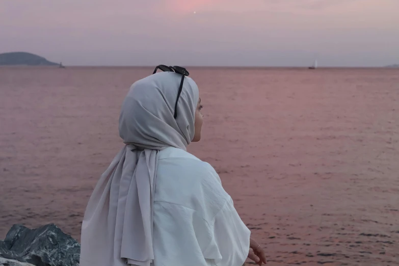 a nun in a white shawl and headscarf staring out over the ocean at sunset