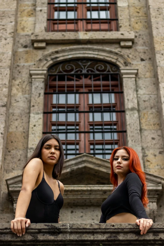 two women are posing on the balcony of an old building