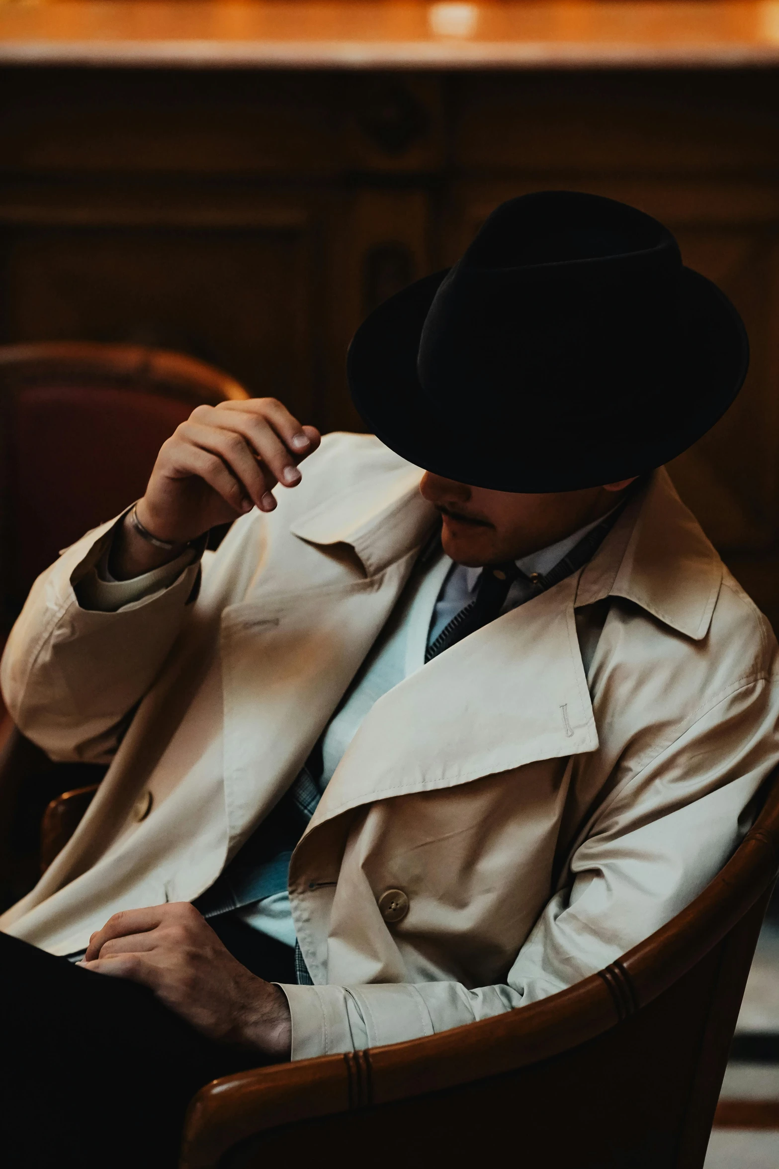 a man wearing a beige trenchcoat and a black hat