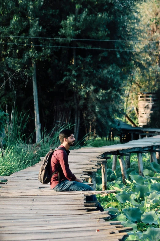 a young man sitting on the edge of a wooden walkway