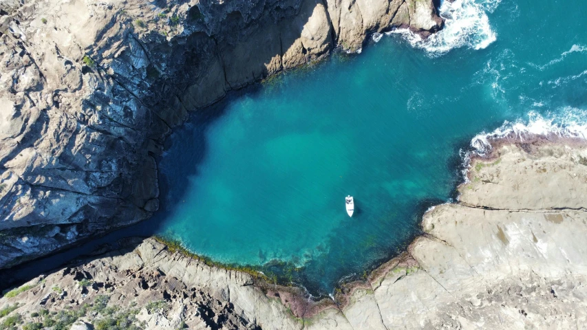 a small white boat is at the blue pool on a cliff