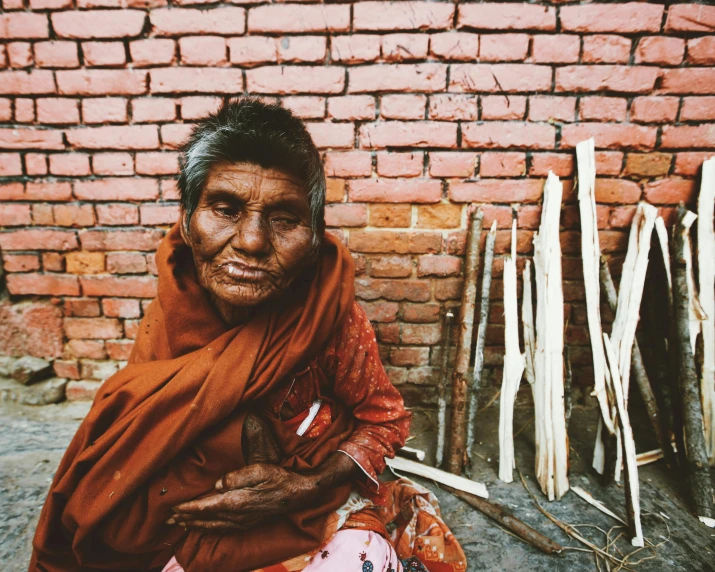 a woman sitting next to a building in front of a brick wall