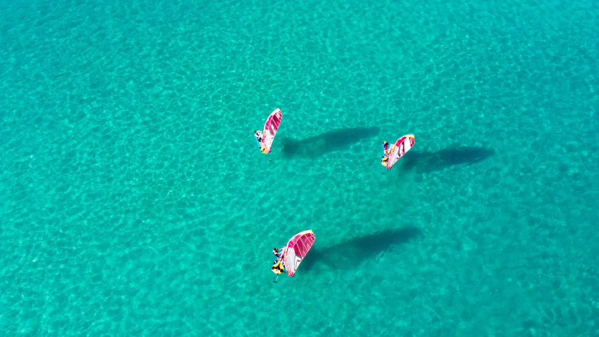 three people riding sail boards in clear blue water