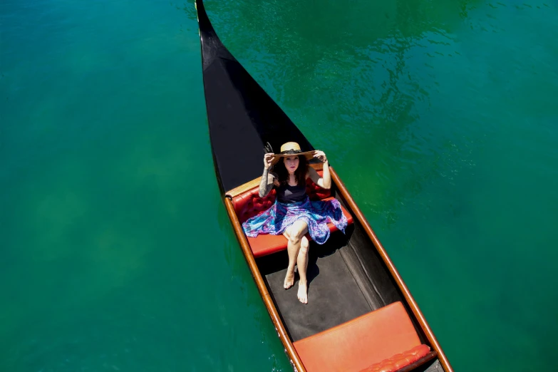 woman in blue dress and hat on small boat in blue green water