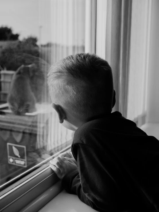 a black and white image of a little boy looking out a window