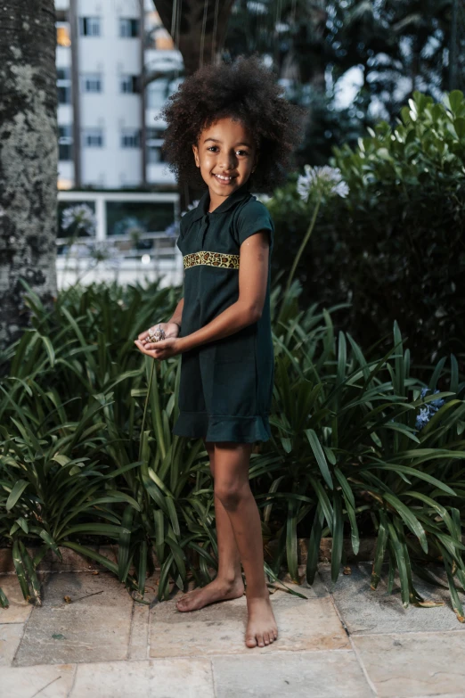 a child poses for a picture while standing next to shrubbery