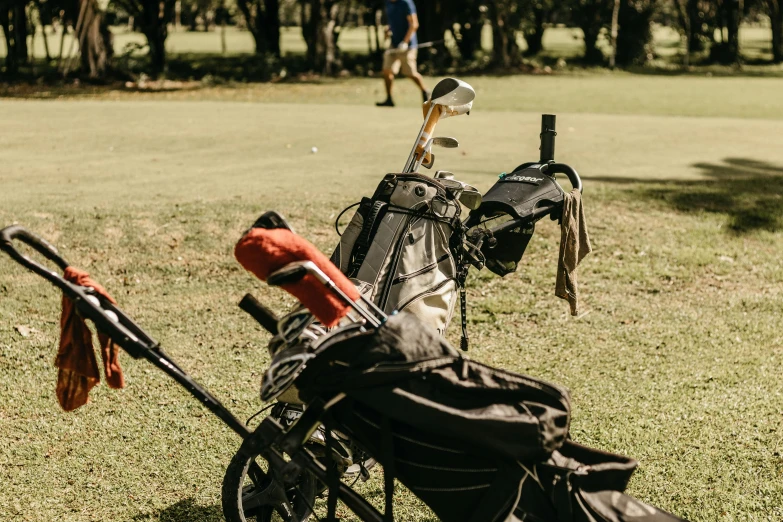 golf equipment on grass, two people in distance, and the two bags have their golf clubs