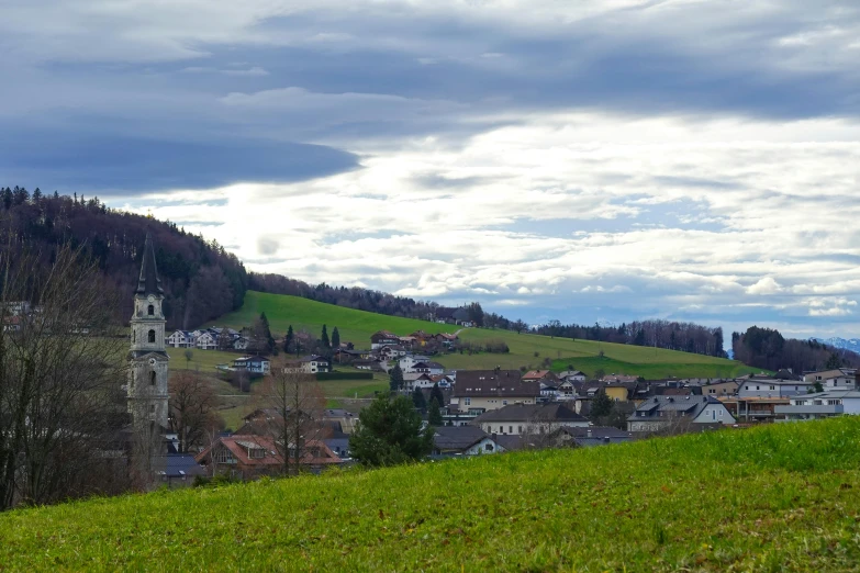 a green mountain with a village under a cloudy sky