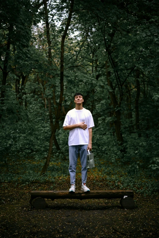 a young man stands on a wooden ledge in a wooded area