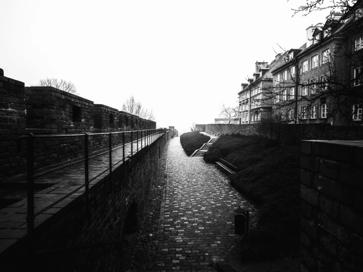 the dark pathway of a sidewalk leads towards two brick buildings