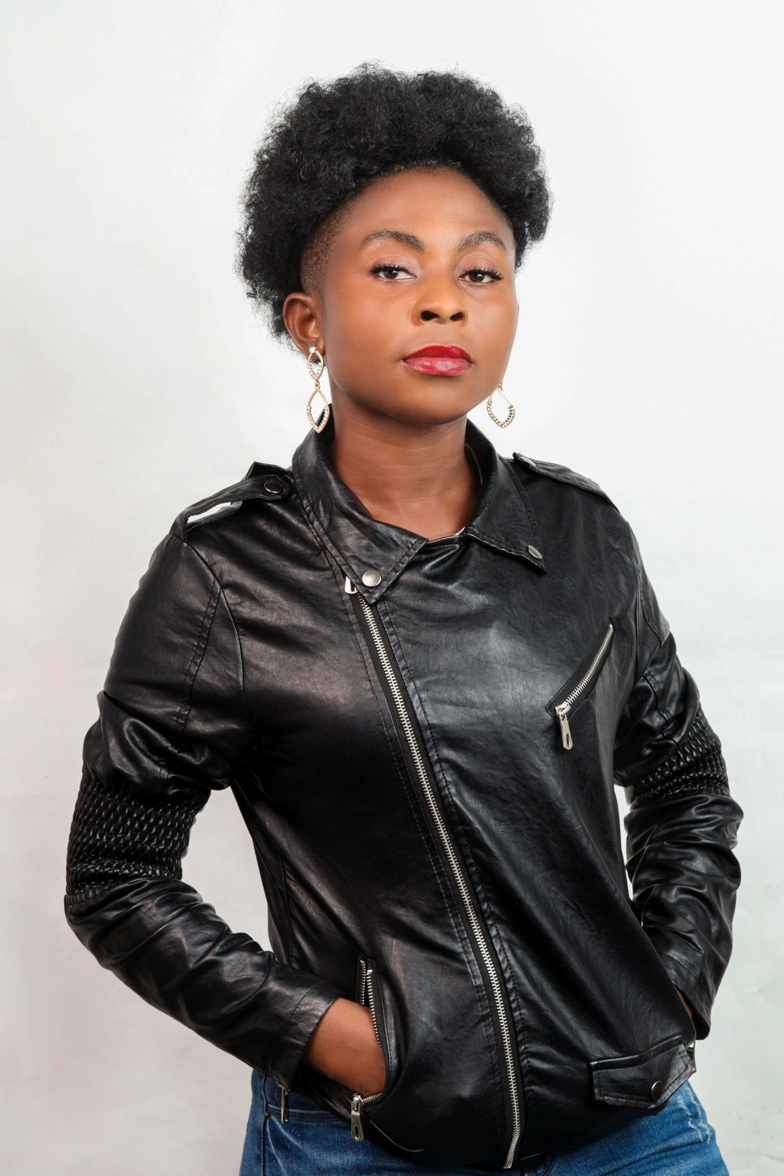 a woman standing up wearing a black jacket and earrings