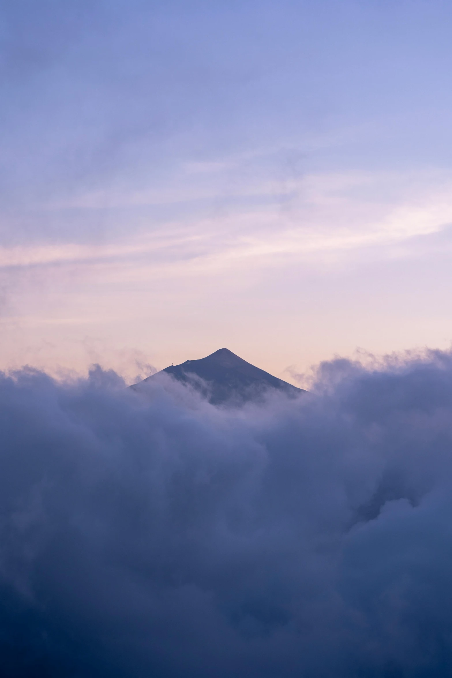 the clouds are gathering below a mountain in the evening