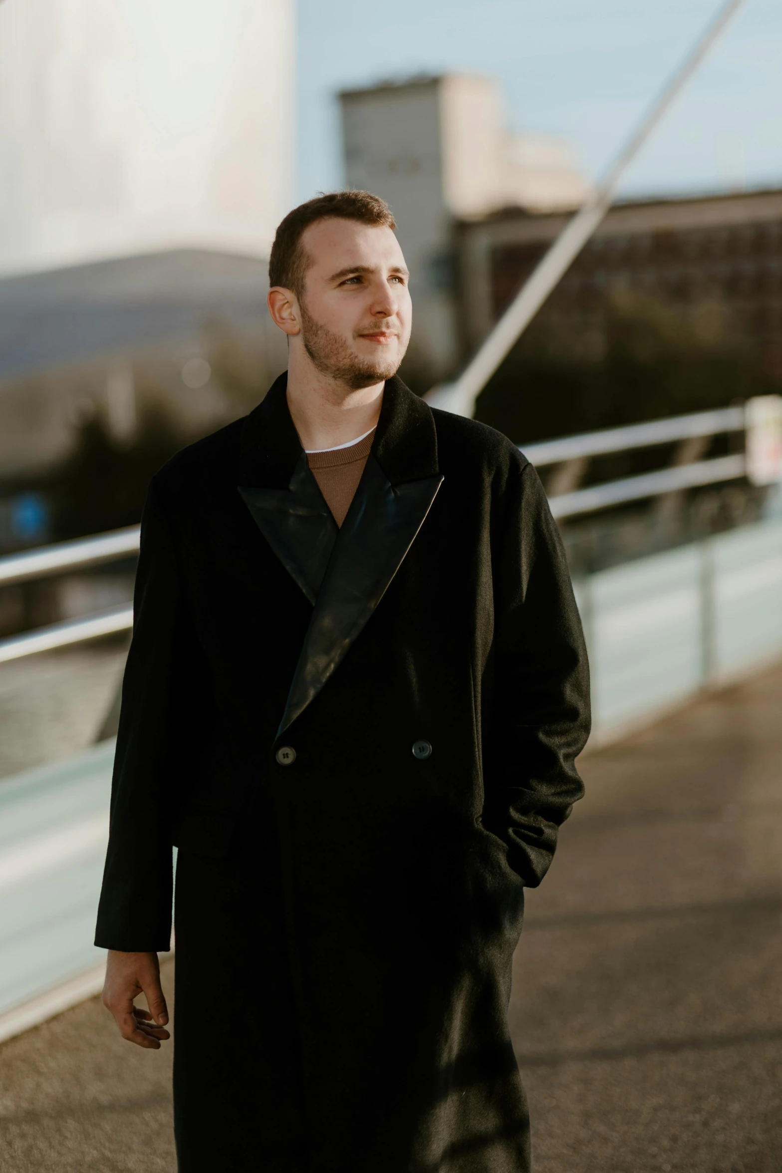 a young man wearing black walks on a walkway in front of a cityscape