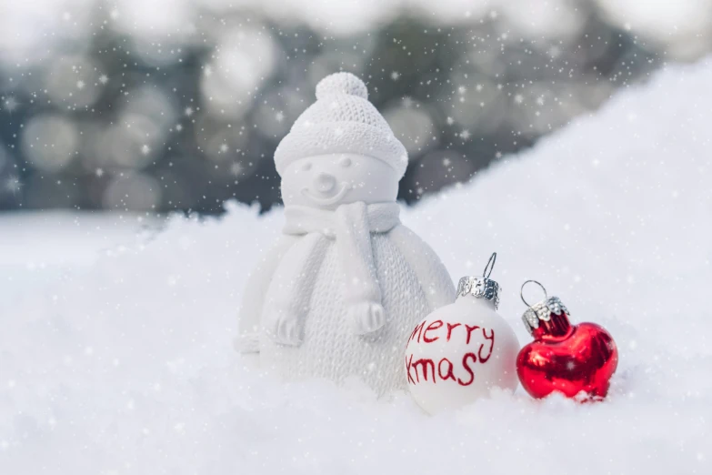 a snowman ornament sitting on the snow next to a christmas ornament