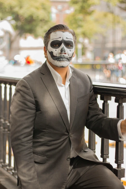 a man with makeup painted on his face and a skeleton like nose sitting on a rail