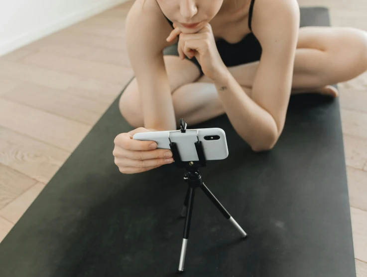 an asian woman kneeling down on a yoga mat with her phone