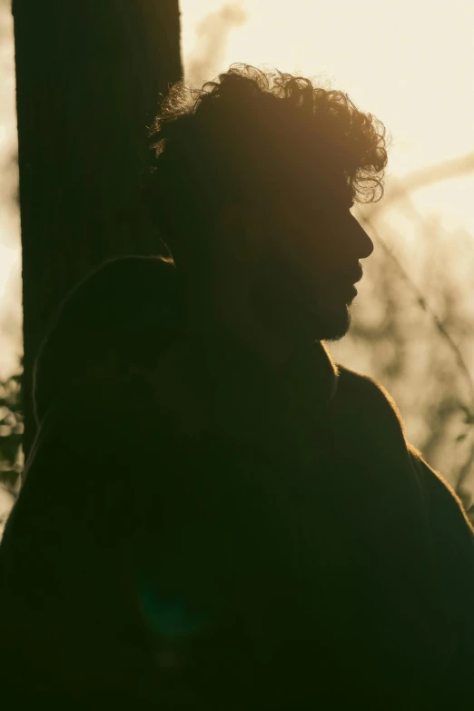 a man standing next to a tree in the sunlight