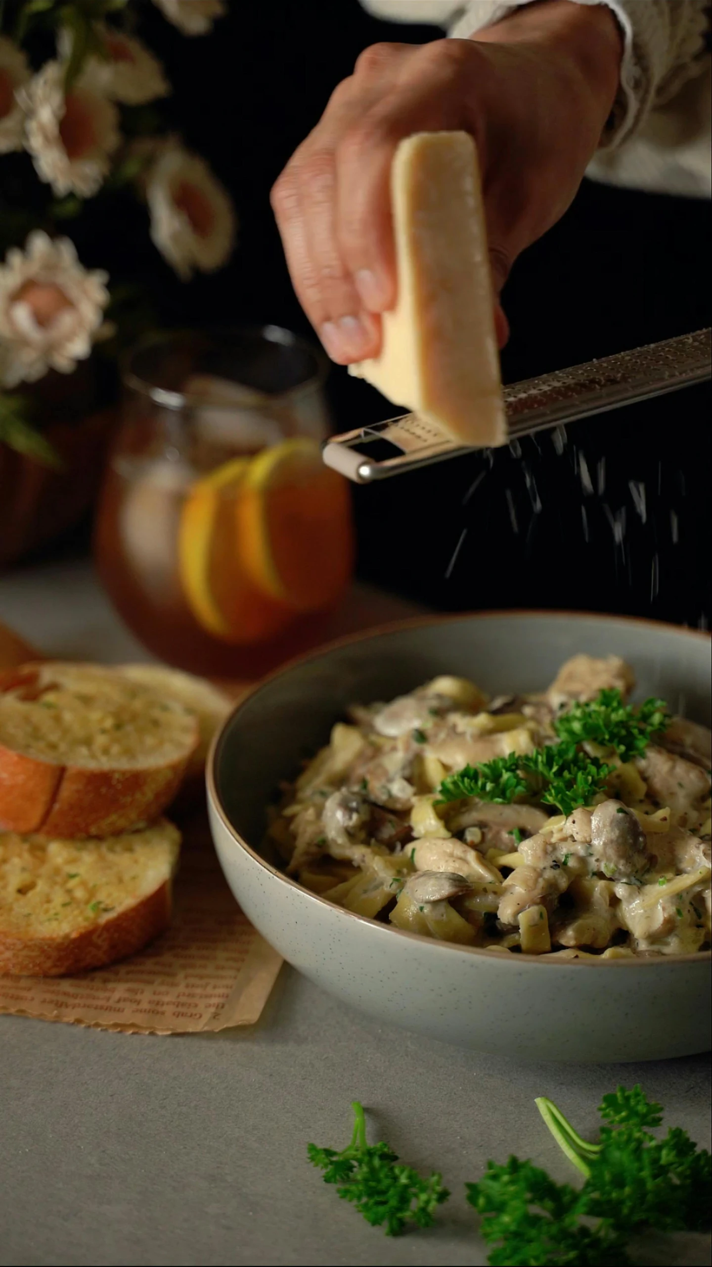 a person sprinkle cheese on a pasta dish with parsley