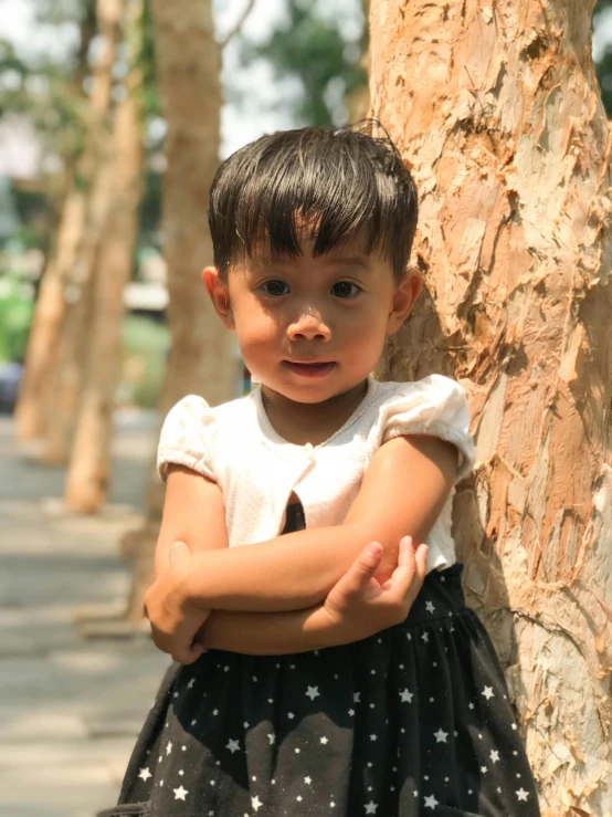 a very cute little girl leaning on a tree