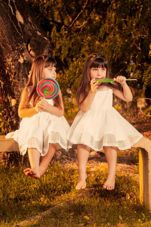 two girls sit on a bench with large lollipops in their hands