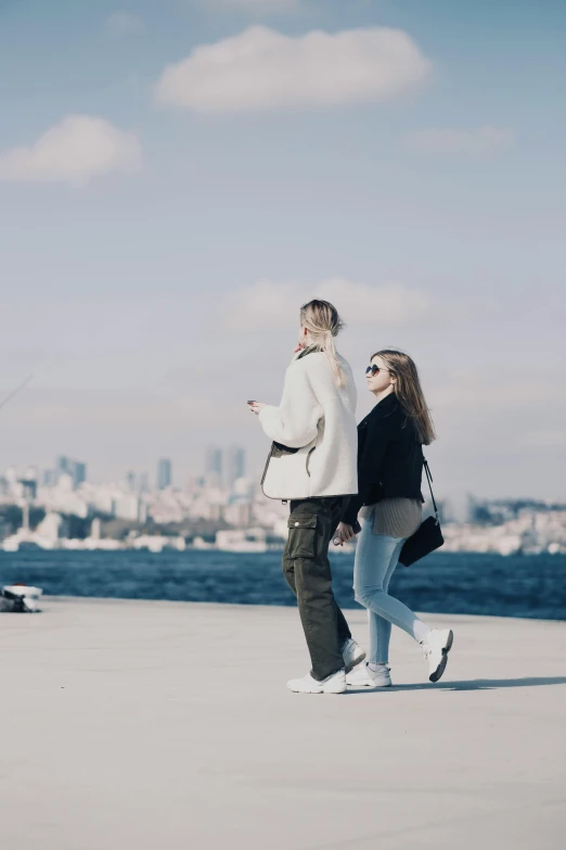 two people are walking along the beach by the water