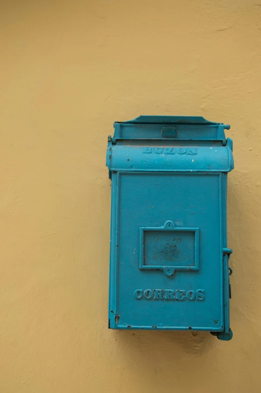 a blue mailbox on a wall in front of a tan building