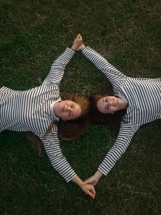 two girls in striped shirts are sitting on the grass