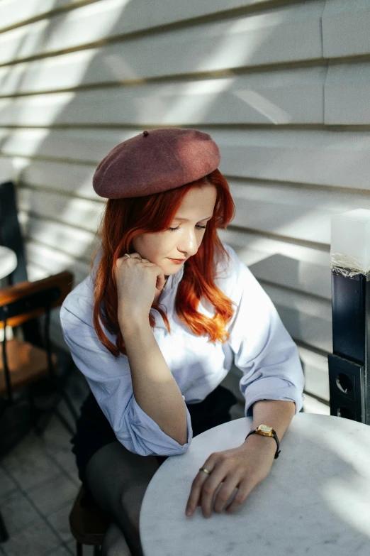 a young red - haired woman leaning on a white table wearing a pink beret