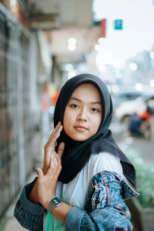 woman in hijab holding up peace sign standing in urban street