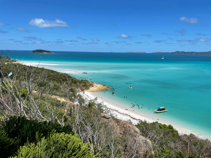 a group of people walk along the beach towards a tropical bay