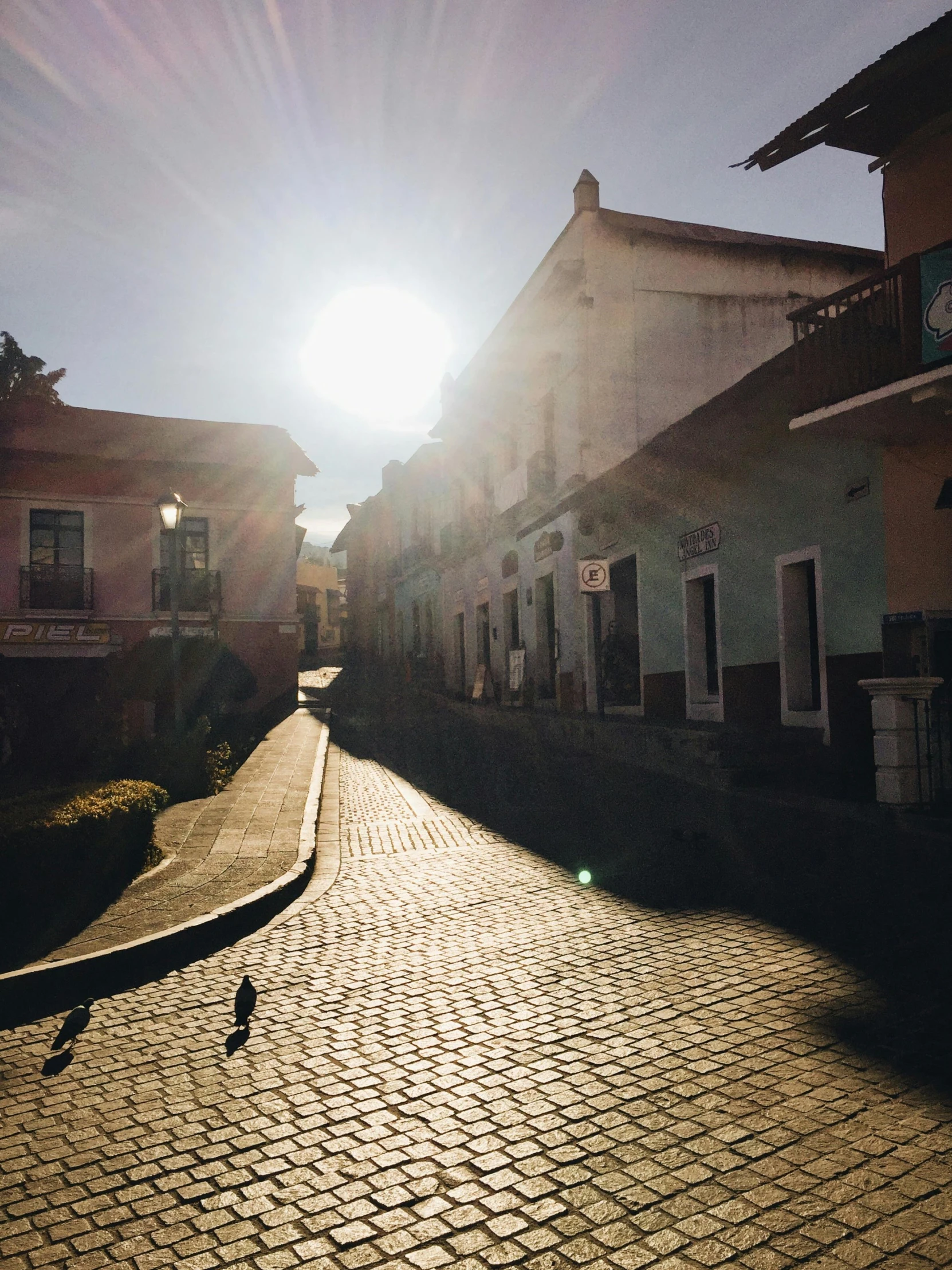 a street in the middle of a building and a sun glaring through the window