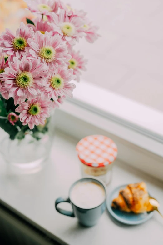 flowers in a vase with a plate and cup sitting on a window sill