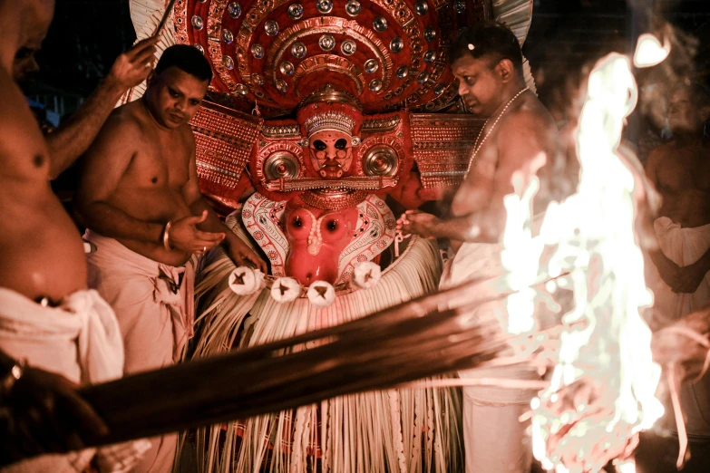 a group of men standing around a fire pit with a man's face painted red and gold