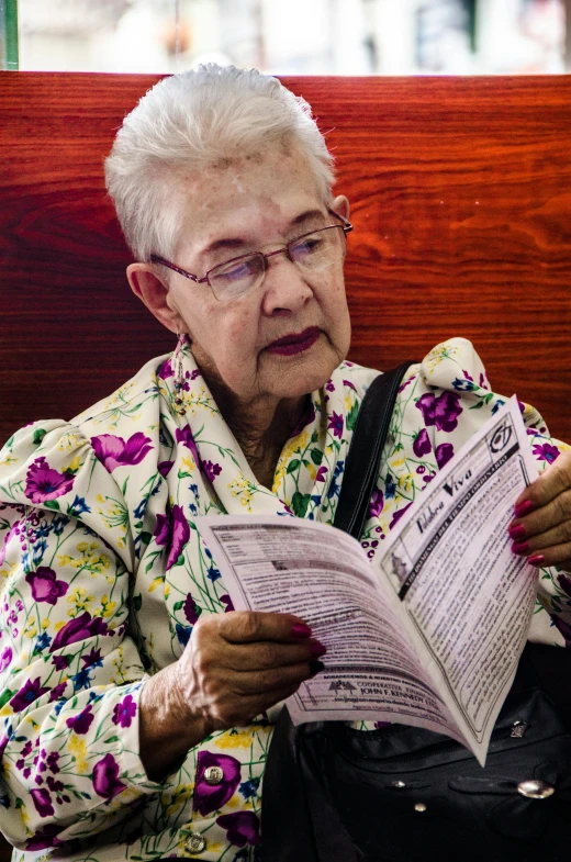 an elderly woman looking at the paper while reading it