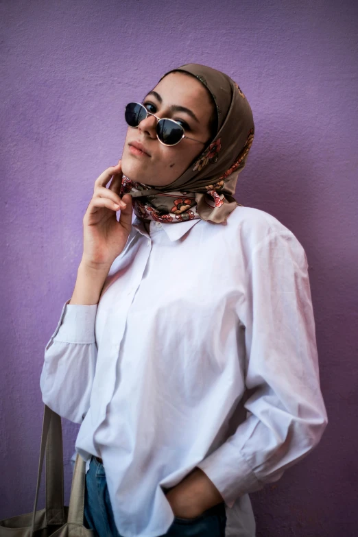 a woman wearing sunglasses and a scarf standing next to a purple wall