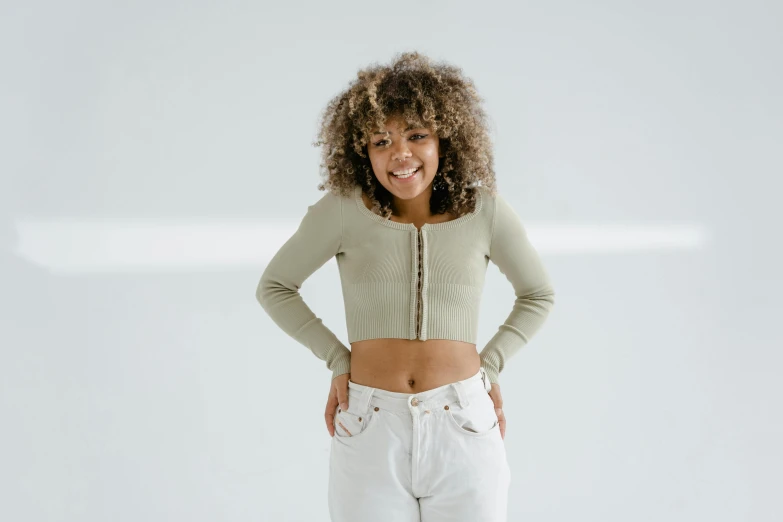 a woman wearing white pants and cropped top standing