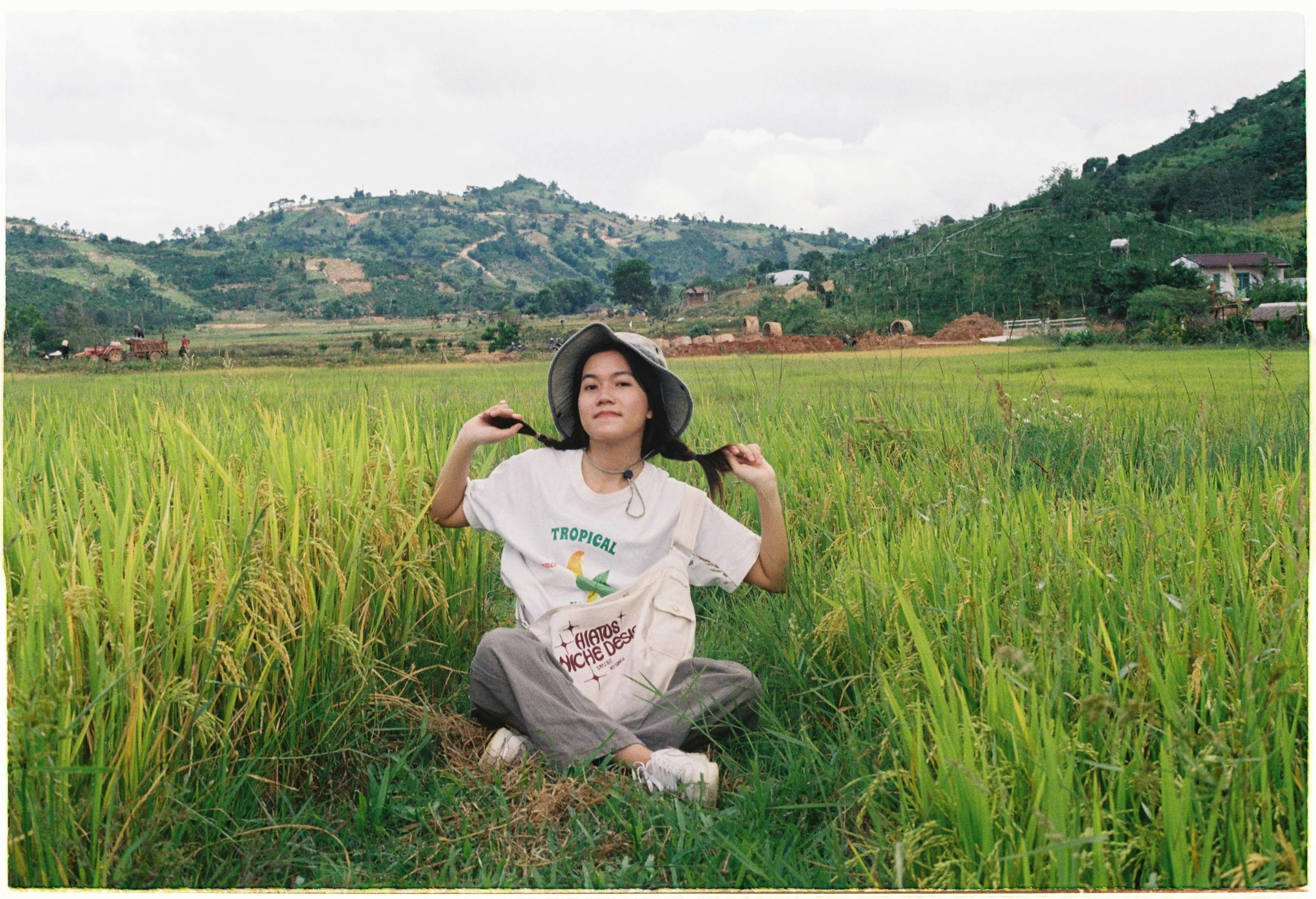 an asian woman sitting in a grass field, holding hair