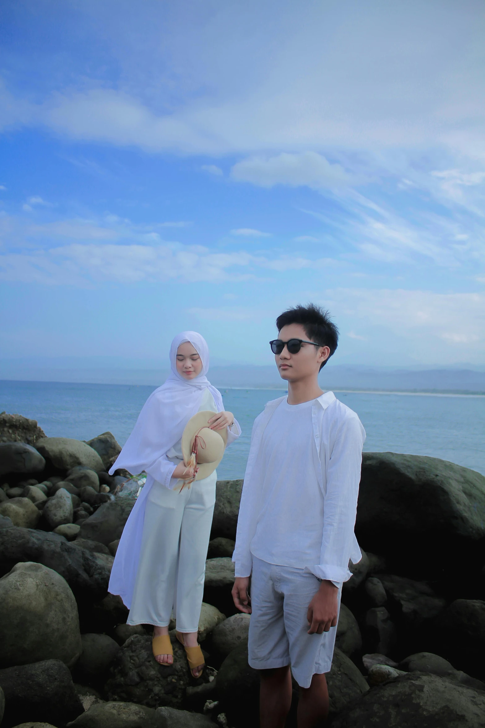 man and woman in white clothing standing on rocks with body in background
