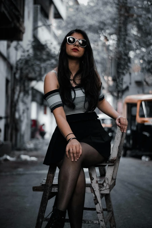 woman wearing black outfit and tights sitting on a wooden chair in the city