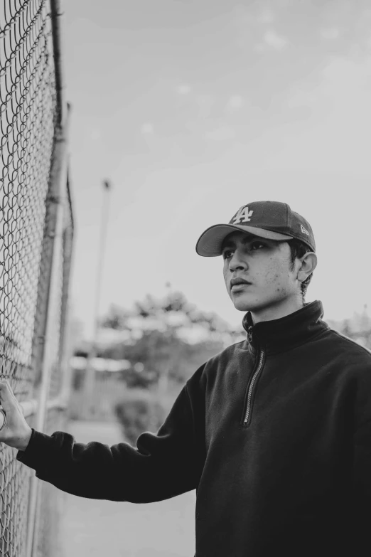 man leaning against the chain linked fence holding baseball mitt