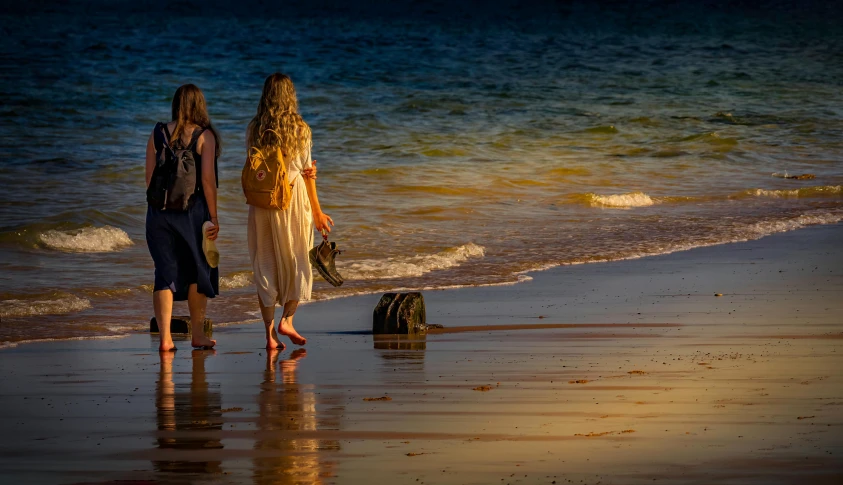 two women walk along a beach with a dog