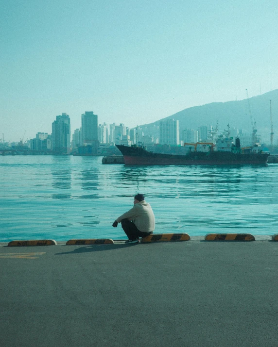 a man sits on a bench in front of the sea watching the ships