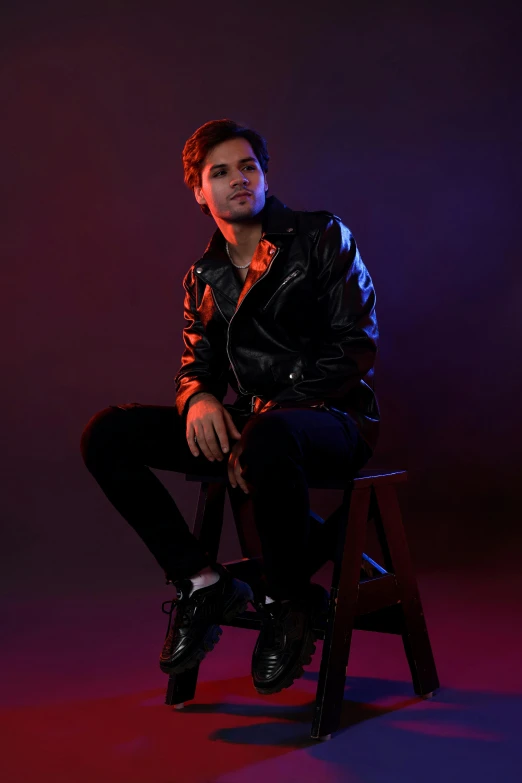 a man with a leather jacket sits on a chair