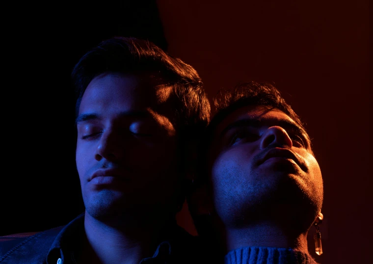 two men in a dark room resting their heads on each other