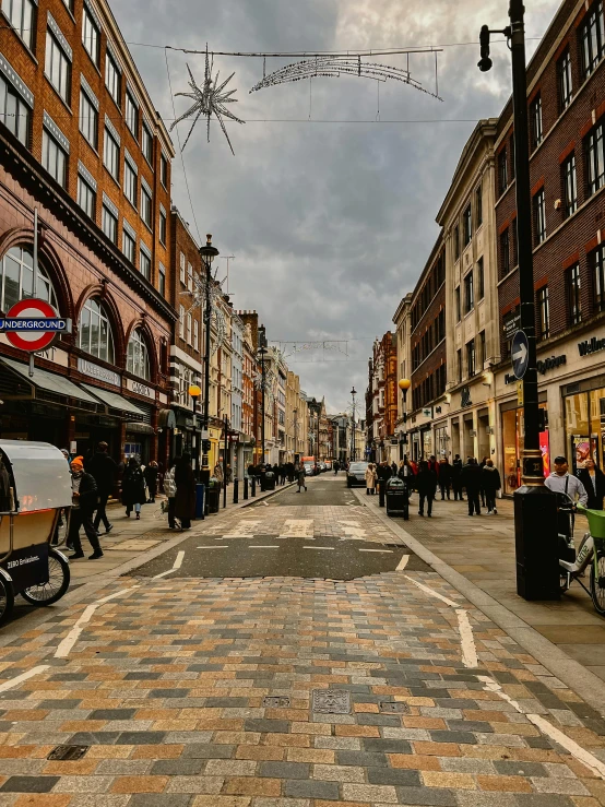 a city sidewalk with cobblestone on one side and several people walking down the other